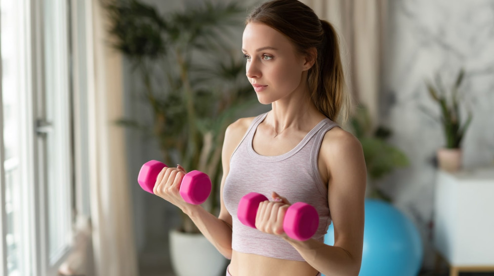 Młoda kobieta w sportowym topie trzyma w dłoniach małe hantle winylowe