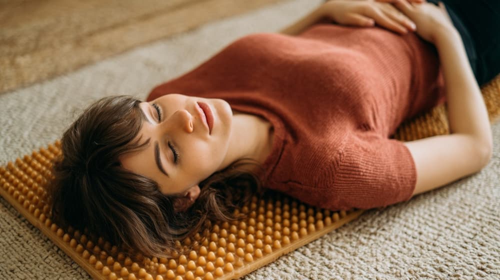 Dziewczyna leży zrelaksowana na macie do akupresury, dłonie oparte na brzuchu, na twarzy spokój i ulga