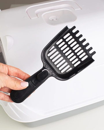 Czarna łopatka do kuwety trzymana nad białą kuwetą dla kota